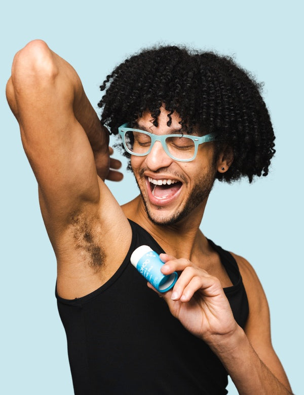 Smiling man applying WooHoo Surf natural deodorant stick to his underarm