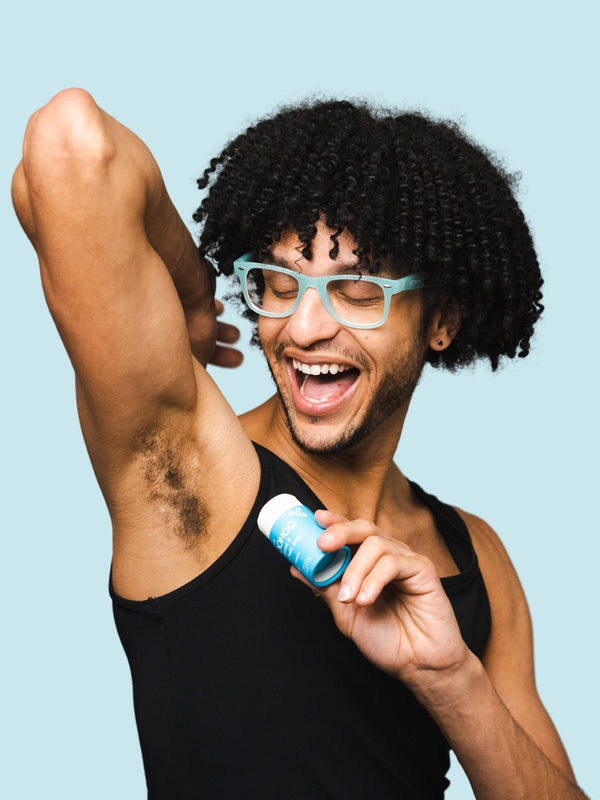 Smiling man applying WooHoo Surf natural deodorant stick to his underarm