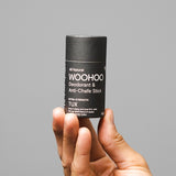 WooHoo Tux deodorant stick held in a hand against a grey background