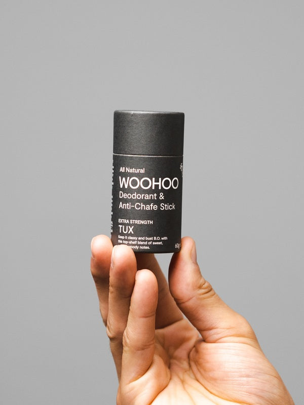 WooHoo Tux deodorant stick held in a hand against a grey background