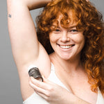 Smiling woman applying WooHoo Tux deodorant stick to her underarm