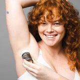 Smiling woman applying WooHoo Tux deodorant stick to her underarm