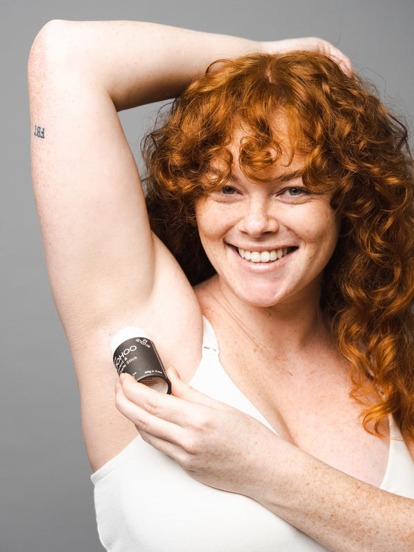 Smiling woman applying WooHoo Tux deodorant stick to her underarm