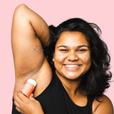 Smiling woman applying WooHoo Urban natural deodorant stick to her underarm