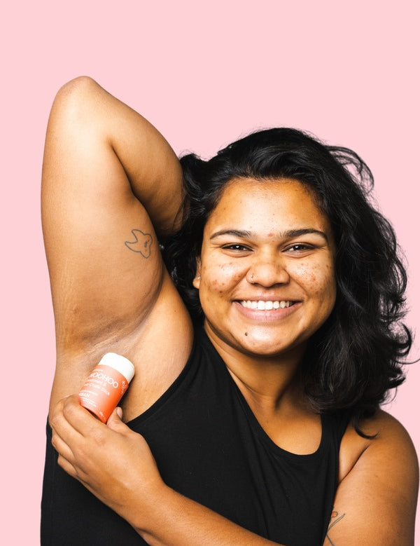 Smiling woman applying WooHoo Urban natural deodorant stick to her underarm
