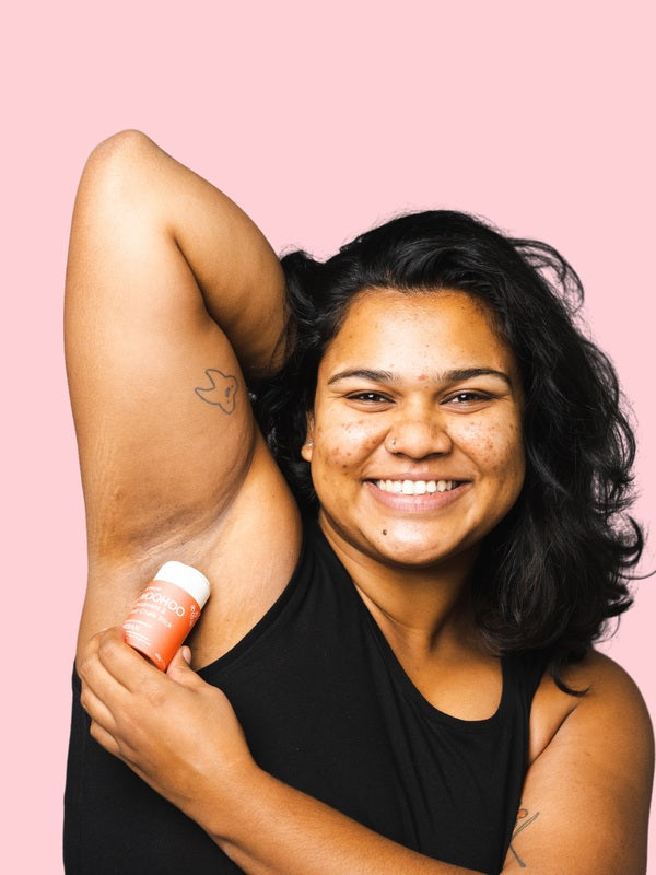 Smiling woman applying WooHoo Urban natural deodorant stick to her underarm