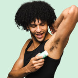 Smiling man applying WooHoo Wild natural deodorant stick to his underarm