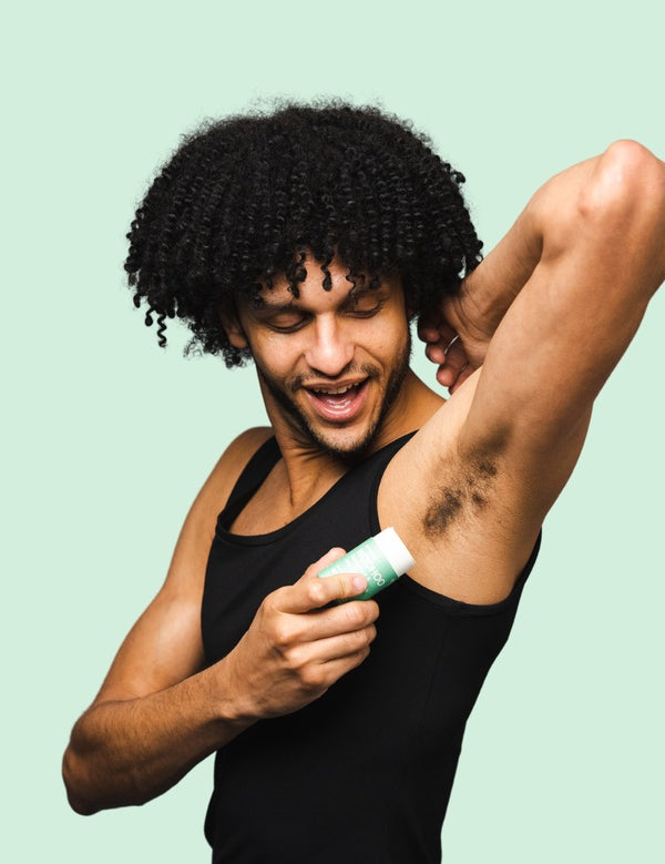 Smiling man applying WooHoo Wild natural deodorant stick to his underarm