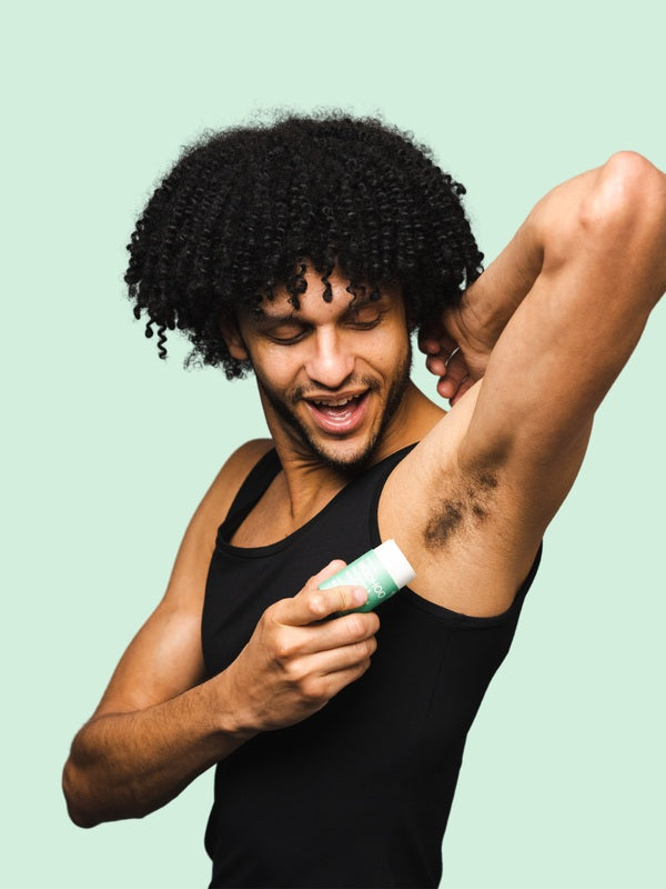 Smiling man applying WooHoo Wild natural deodorant stick to his underarm