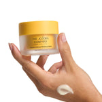 Hand holding a jar of The Jojoba Company Jojoba Intense Moisture Balm with a smear of balm