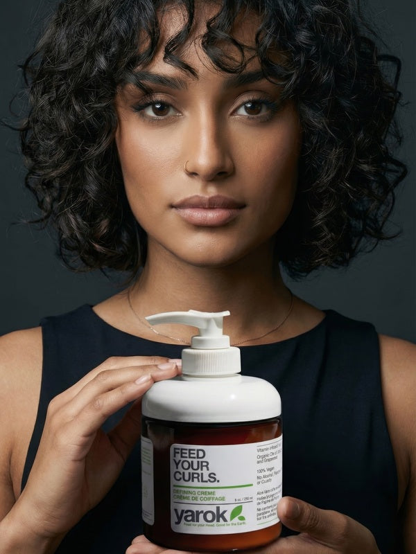 Woman with curly hair holding Yarok Feed Your Curls Defining Crème