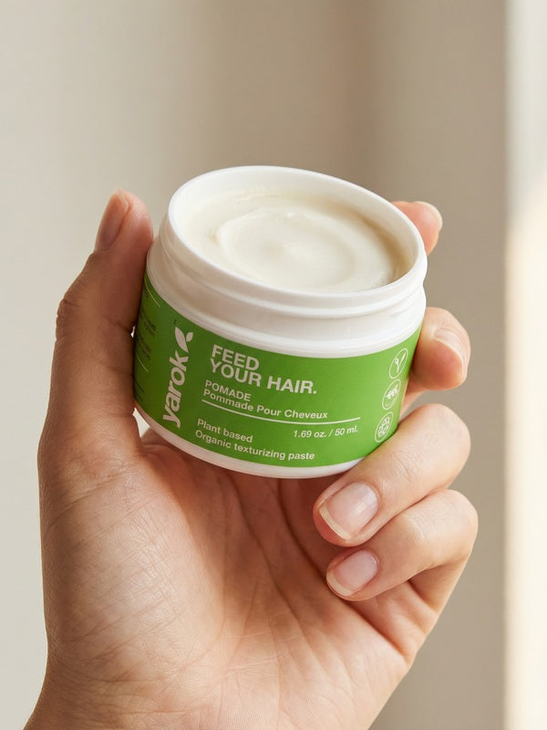 Hand holding an open jar of Yarok Feed Your Do Styling Pomade