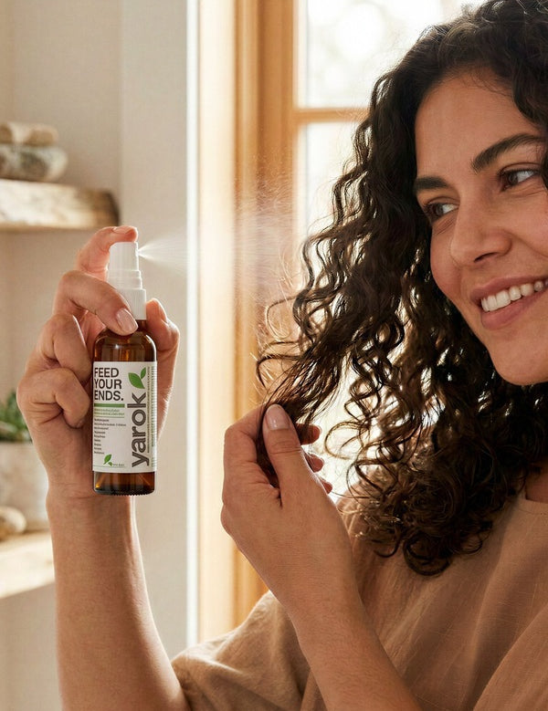 Woman applying Yarok Feed Your Ends Leave-In Conditioner to curly hair