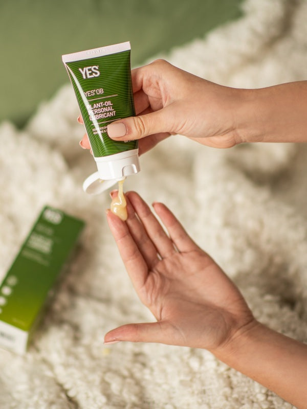 Hands dispensing YES OB Plant Oil-Based Lubricant beside a bed